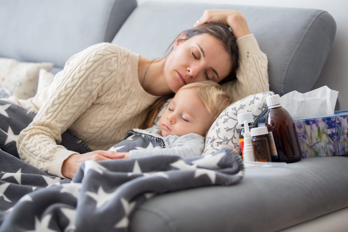 Mutter die auf dem Sofa neben ihrem kranken kleinen Kind liegt und beide schlafen